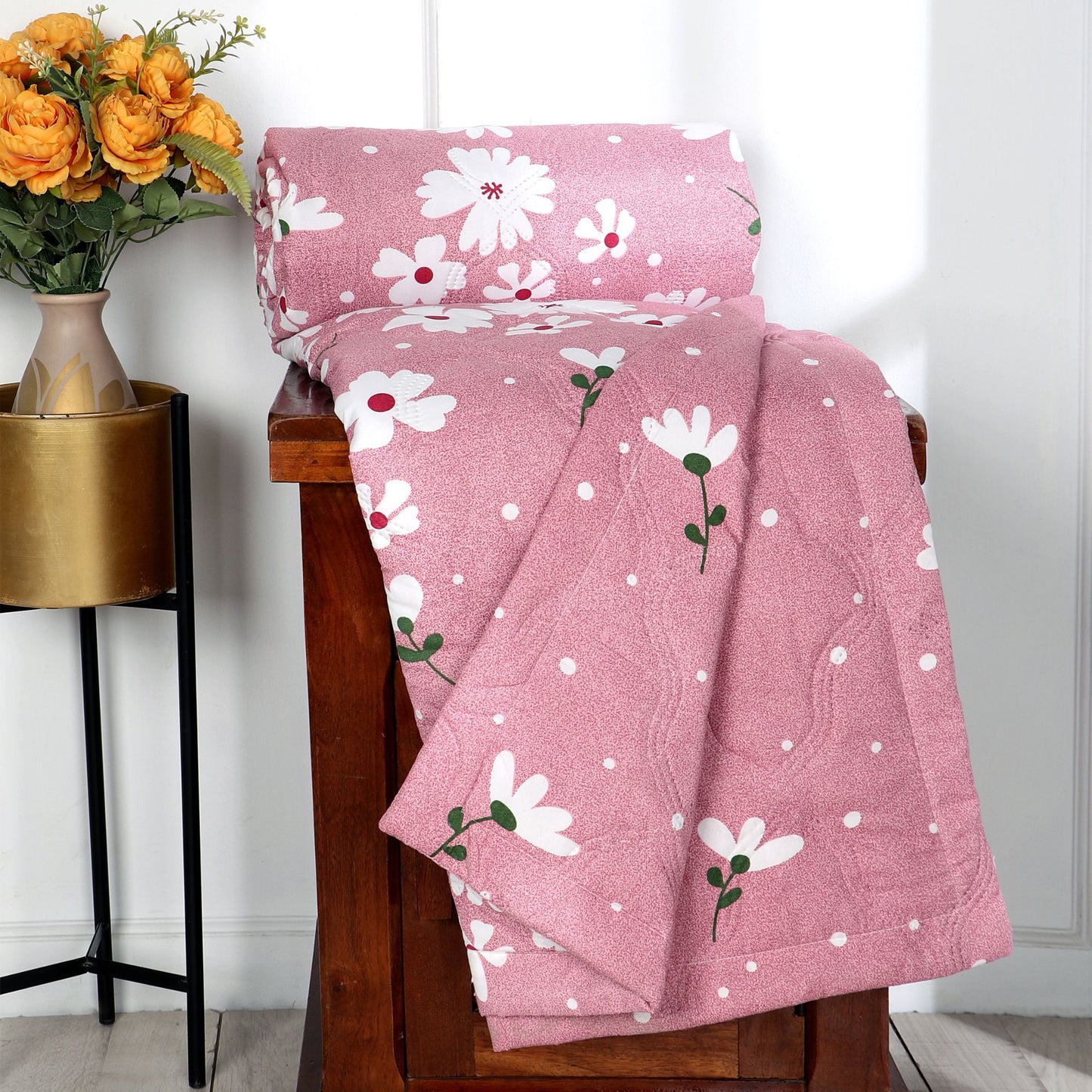 Pink floral-patterned comforter on a wooden bench with a vase of flowers in the background.