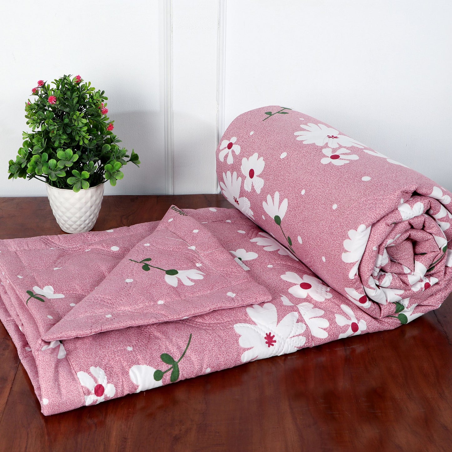 Pink floral blanket on a wooden surface with a plant in the background