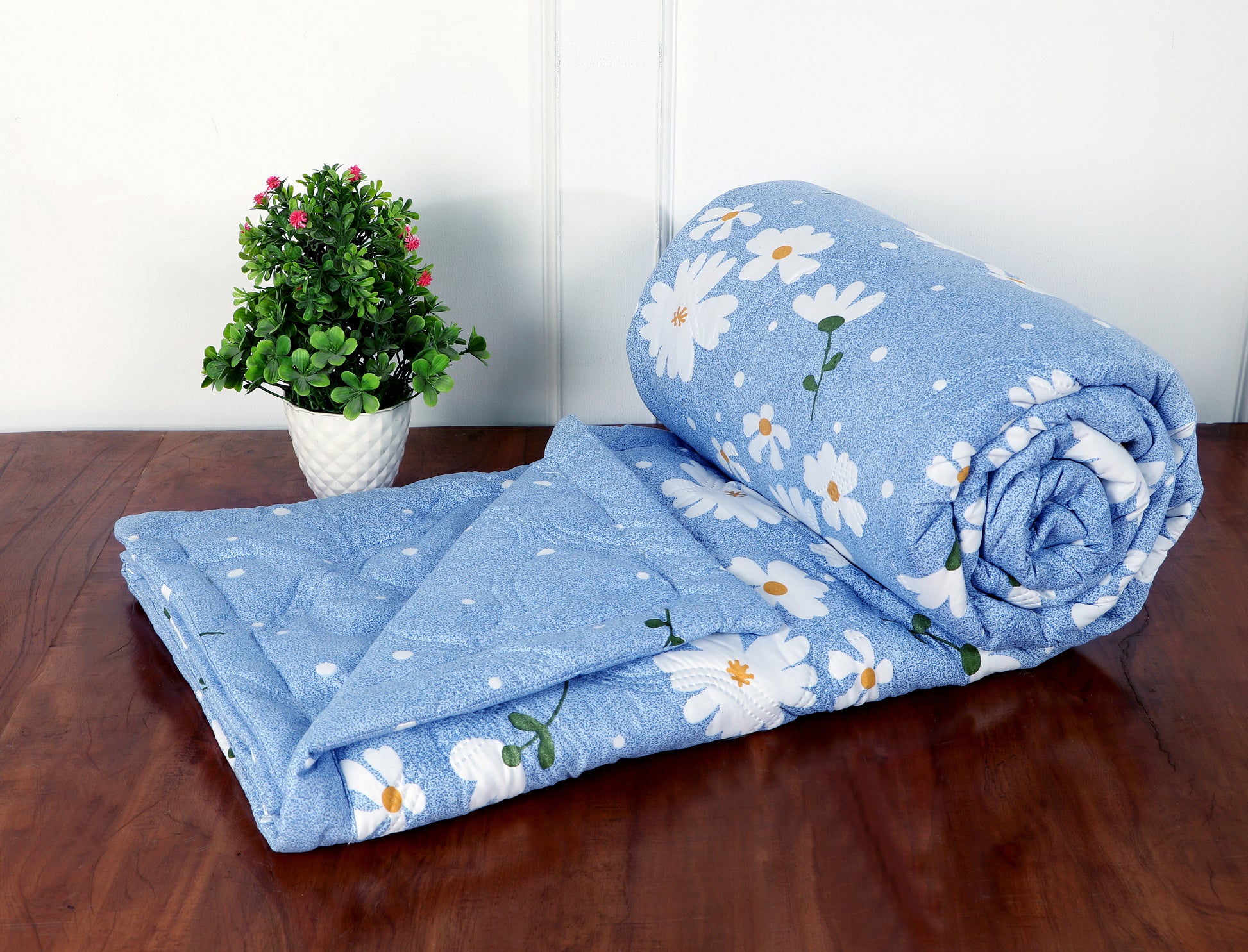 Blue floral-patterned blanket on a wooden surface with a plant in the background